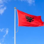 Albania flag. Albanian flag on a pole waving on blue sky background