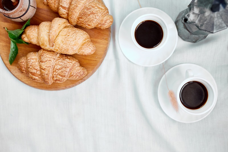 Two coffee cups and Italian coffee maker with croissant.